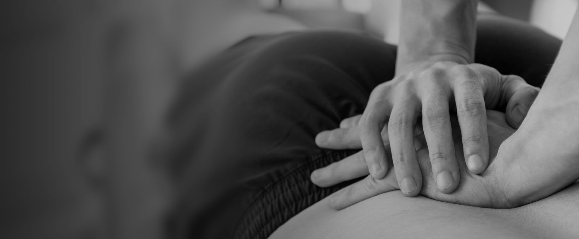 Schwarz-weiß Aufnahme von Händen, die eine therapeutische Behandlung auf der Schulter durchführen